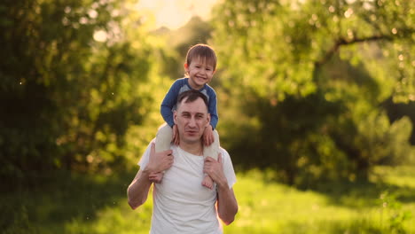 A-child-sitting-on-the-neck-of-his-father-while-walking-in-summer-field-at-sunset.